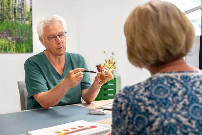 Ein Azrt erklärt etwas einer Patientin mittels eines Modellherzens.