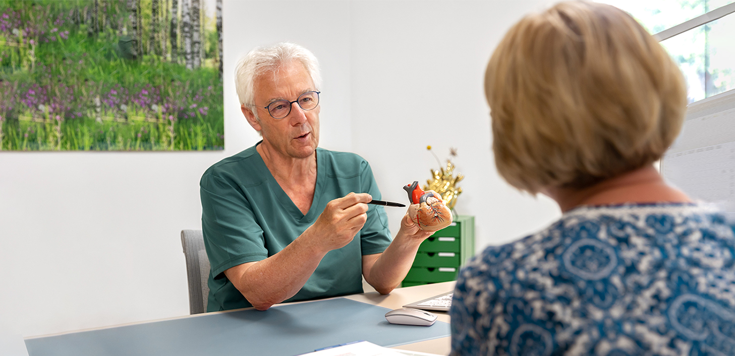 Ein Azrt erklärt etwas einer Patientin mittels eines Modellherzens.